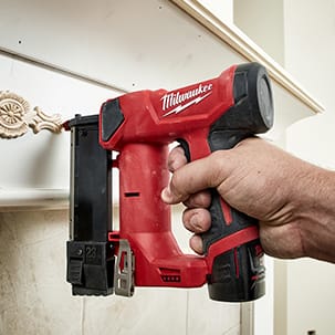 Man uses M12 23 Gauge Pin Nailer with dry-fire lockout feature to ensure damage-free nailing on decorative fireplace molding.