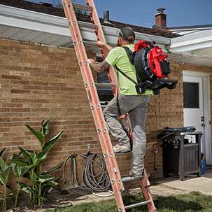 Plumber climbs ladder to the roof on a residential jobsite with M18 120' Pipeline Inspection System on his back.