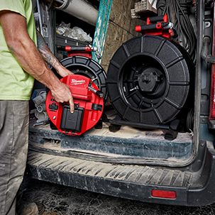 Plumber swaps reel on control hub of the Milwaukee M18 120' Pipeline Inspection System in back of van.