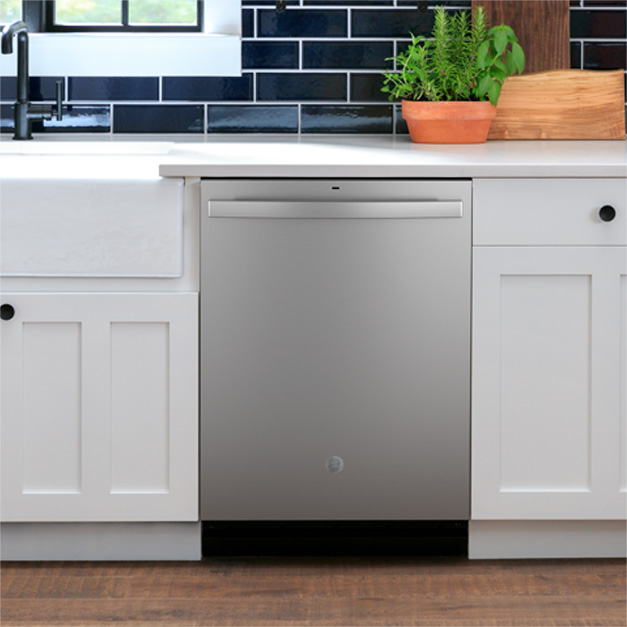 GE stainless steel dishwasher in vignette with white cabinets, sink and plants