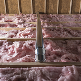 An attic is shown, with the vent running above the insulation and out of the house.