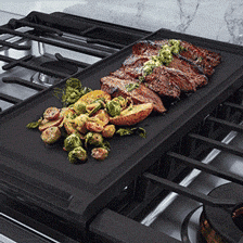 Vegetables cooking on cast iron griddle shown on gas cooktop.