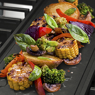 Vegetables cooking on an integrated griddle on a gas cooktop.