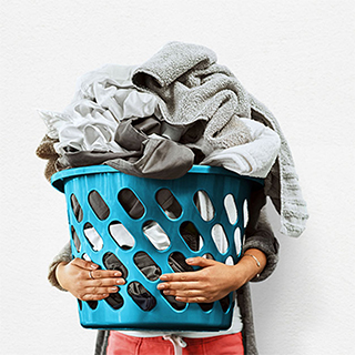 Image of someone holding blue laundry basket full of clothes.