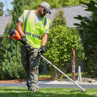 Man trimming grass with PAS string trimmer attachment