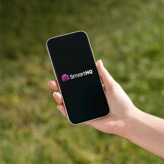 The SmartHQTM app on a phone in the foreground and an outdoor scene  in the background.