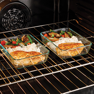Two glass containers sit inside the oven as leftover chicken, rice, and vegetables are freshly reheated.