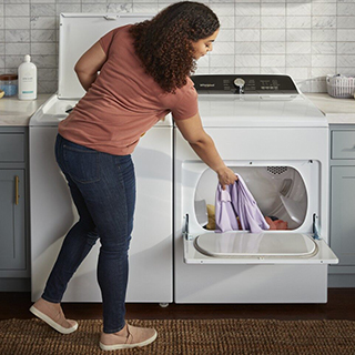Woman pulling fresh laundry out of a White Whirlpool Dryer